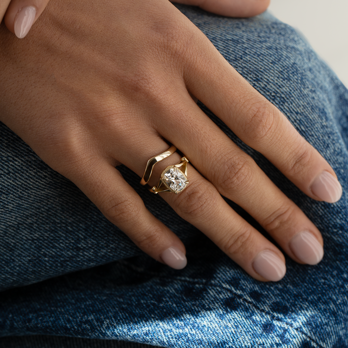Hand wearing a gold ring with a diamond on a denim background