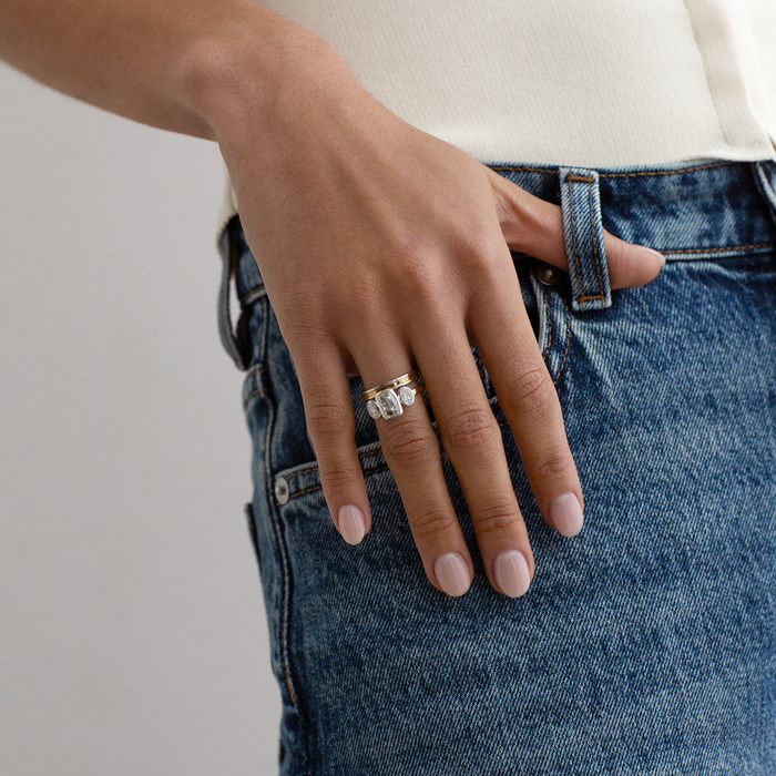 A close-up of a person's hand resting on their blue denim jeans, wearing a silver ring with a large clear gemstone cluster.