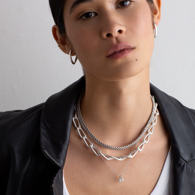 Person wearing multiple silver necklaces on a plain background