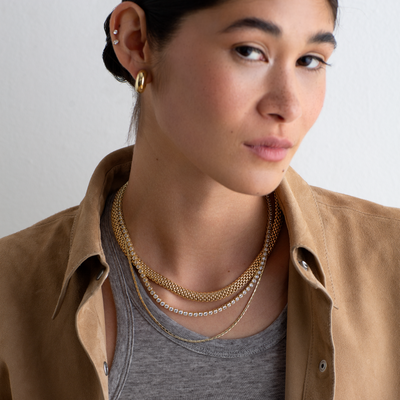 Woman wearing a brown jacket and gold necklaces against a plain background
