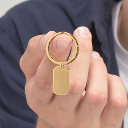 Gold keychain with a tag held by a hand against a neutral background