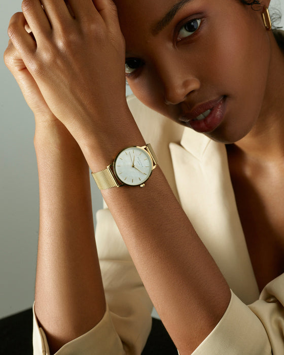 Woman wearing a gold watch with a neutral background