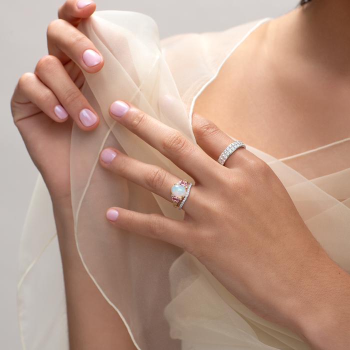 Close-up of a hand wearing a ring with a diamond, holding a sheer fabric against a neutral background.