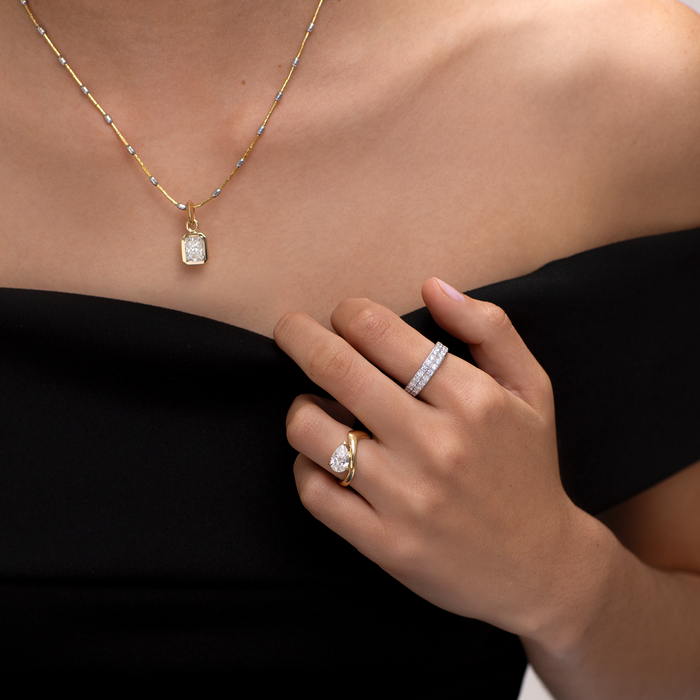 Close-up of a person wearing gold jewelry including a necklace, ring, and bracelet on a plain background.