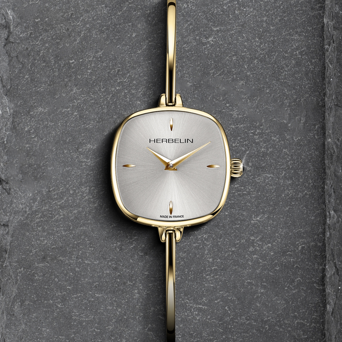 Gold watch with silver face on a dark gray stone background