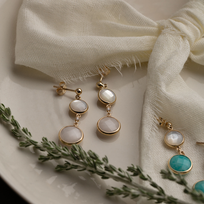 Gold earrings with white and turquoise stones on a textured fabric background