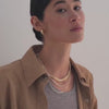 Woman wearing a brown jacket and gold necklaces against a plain background