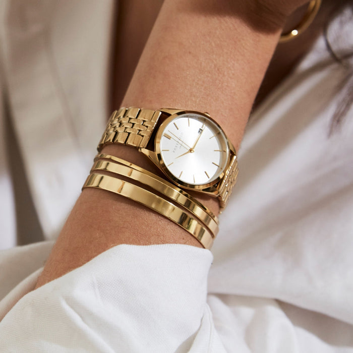 Gold watch and bracelets on a wrist with a blurred background