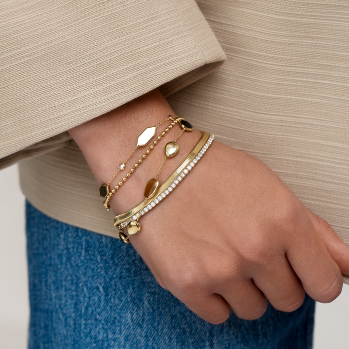 Hand wearing multiple gold bracelets with a neutral background